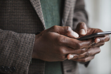 Obraz na płótnie Canvas Close-up of African businessman in suit typing a message on his mobile phone