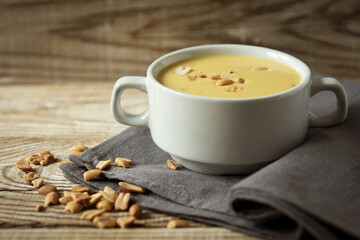 mashed peanut soup with coconut milk in a white plate on a wooden background and a linen napkin
