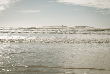 Gentle ocean waves washing a beach in Morocco, Africa. A small rocky island with a lighthouse seen in the distance. 