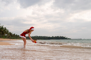 Girl dressed as Santa Claus on a tropical beach with a gift box.