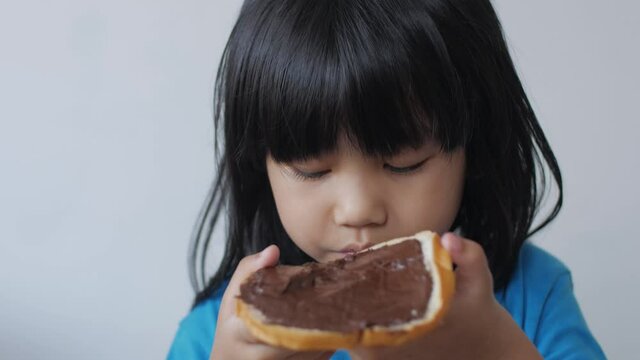 Asian little baby girl eating bread with chocolate cream, kid enjoys breakfast or snacks of toast with jam