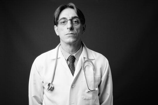 Mature handsome Italian man doctor against gray background