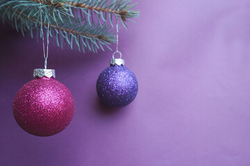 two round shiny purple and lilac Christmas balls hang on the Christmas tree on a lilac background in nightshade colors . Symbols of Christmas and New year