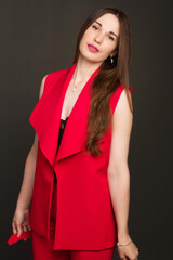 Studio portrait of a young woman in a red suit on a dark background.
