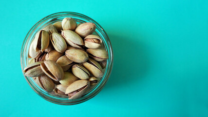small round transparent glass jar filled with pistachios top view on a blue background