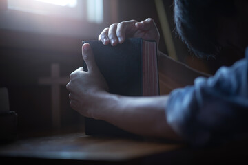 Close up hands of youg male praying with holding the holy bible on wooden table in morning. Christian worship concept.