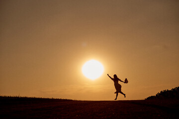 Silhouette of a woman running towards the sun with outstretched hand.