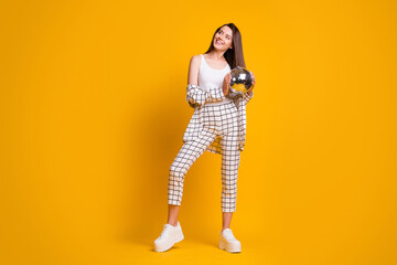 Fototapeta na wymiar Full size photo of nice cute brown hair girl hold disco ball wear checked suit white tank-top shoes isolated over yellow background