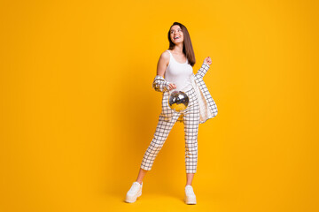 Full size photo of positive nice brown hair girl hold disco ball dance wear suit shoes isolated over yellow background