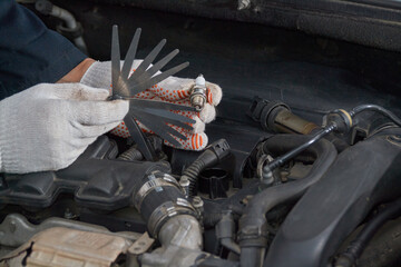 A man with gloves checks the spark plug gap with a feeler gauge - obrazy, fototapety, plakaty