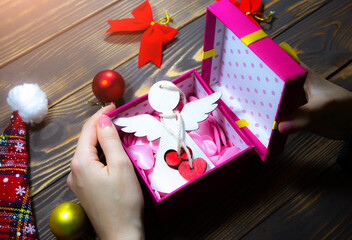 Woman is packing Christmas presents. Wooden angel in hearts. Decorations on wooden table. Happy new year greetings. Cozy mood and festive time. Copy space place.