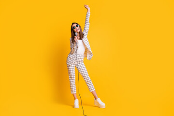 Full length body size photo of girl holding mic singing keeping hand up smiling wearing sunglass isolated on vibrant yellow color background