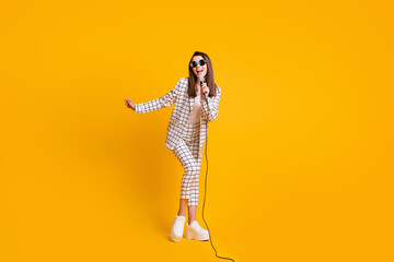 Fototapeta na wymiar Full length body size photo of girl performing with microphone on festival stage wearing sunglass isolated on bright yellow color background