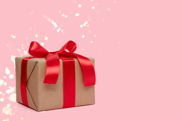 Gift box tied with red ribbon on a pink background with place for text. Holidays composition with shiny glittering bokeh.