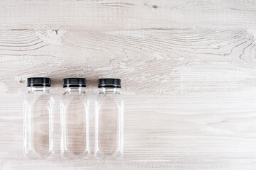 Three plastic transparent bottles with a black cap on a wooden table. There is a place for your logo. Copy space.