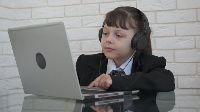 Office work with music. A little boss in a suit work on computer and listen the music in headphones.