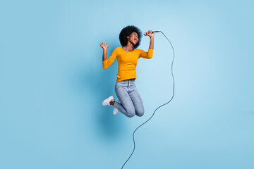 Photo portrait full length of singing woman holding mic in one hand jumping up isolated on pastel...