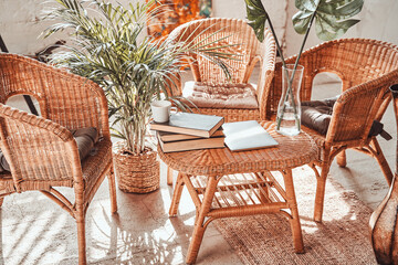 Simple and soft living room in daytime with bamboo armchairs and table with books and laptop on it.