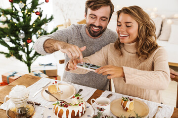 Cheerful couple taking photo on cellphone while having Christmas dinner