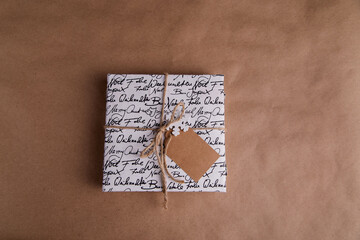 
A gift on a brown background lies, decorated with a twine and a wooden snowflake and a card for an inscription, a laconic photo, stylish minimalism
