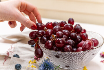Woman's hand picking one red grape on a crystal bowl