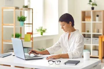 Young business woman sitting and working on laptop in office