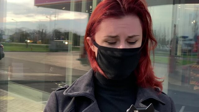 Sad portraid of young woman in black face mask holding phone and looking at you