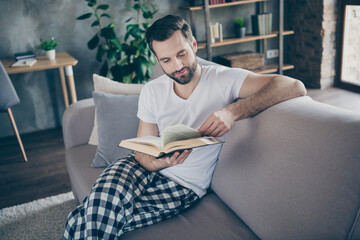 Photo of focused guy sit divan have corona virus quarantine vacation read book wear checkered plaid pant trousers white t-shirt in house indoors