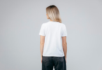 Back of stylish blonde girl wearing white t-shirt posing in studio
