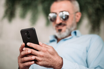 Portrait of middle age man with beard and with sunglasses looking at the phone.