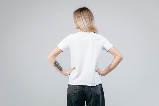 Back of stylish blonde girl wearing white t-shirt posing in studio