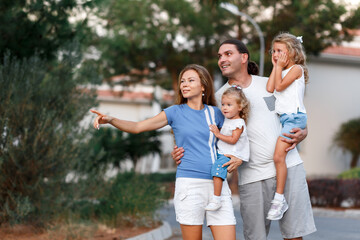 Fototapeta premium Beautiful family portrait, mom, father, small daughters, smiling outside next to their new house with sunset. Consept of new life in new house, life achivements.