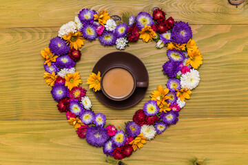 Image of cup of coffee in heart shape made of beautiful flowers  on wooden background.