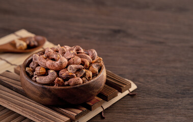 Cashew nuts with peel in a wooden bowl on wooden tray and table background, healthy raw food plate.