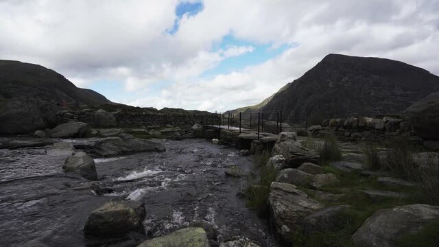 Llyn Idwal lake waterfall beneath a bridge with a cloudy view of the mountains