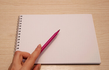 Left female hand holds a purple marker and shows in a clean white notebook
