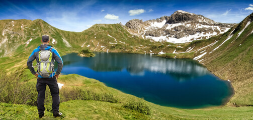 Hiking Man standing at remote lake up high in the alpine mountains. Alps, Bavaria, Schrecksee.
