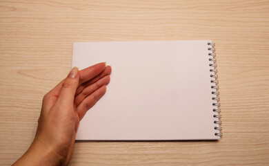 Obraz premium Female left hand lies on a white blank notebook against a wooden background