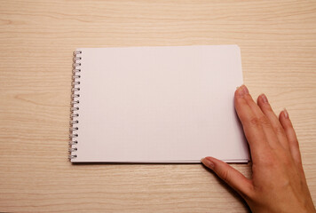 Obraz premium Female left hand lies on a white blank notebook against a wooden background