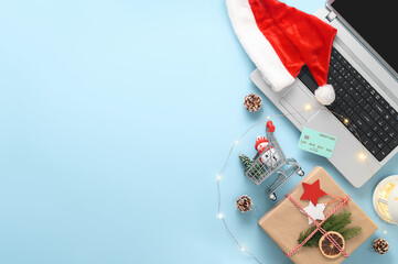 E-commerce and electronic payments concept. Christmas online shopping theme. Top view of laptop, credit card, gift box, shopping cart and Santa hat on a pastel blue background. Copy space, flat lay
