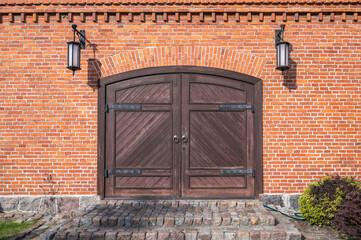 Old wooden gates with iron loops, granite stone steps and lamps on the sides in the red brick wall,...