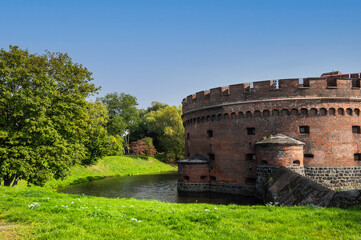 Old fortress with red brick and granite, loopholes, water moat and a lawn with trees against the blue sky, copy space