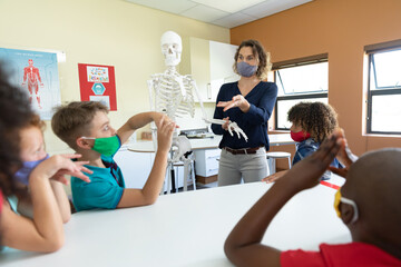 Female teacher wearing face mask using human skeleton model to teach students in class