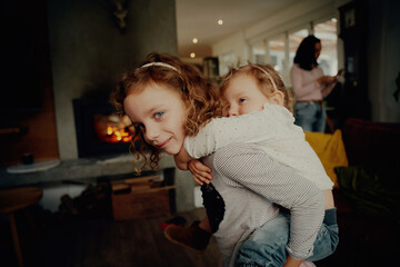 Cute little girl giving younger sister a piggyback ride at home