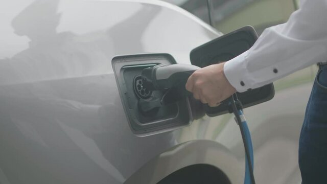 Close up of a modern electric car charger being attached to a silver electric car by a male person wearing a white shirt. Shot in slow motion in 4K.