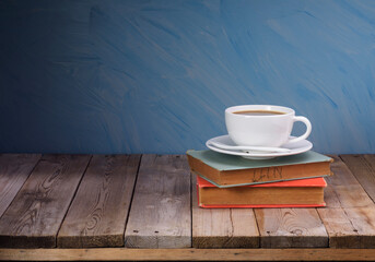 White coffee cups and dark black coffee are placed on a pile of old books on an old wooden table. Blue wall background