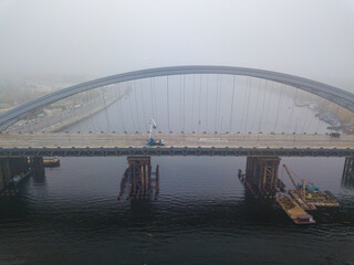 Aerial drone view. Construction of a cable-stayed bridge across the river in dense fog.