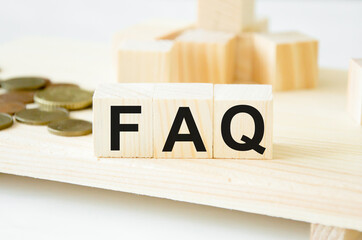  Wooden cubes with the inscription FAQ in the background of coins and cubes. Frequently asked...