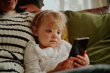 Cute toddler child having fun using smartphone relaxing on couch