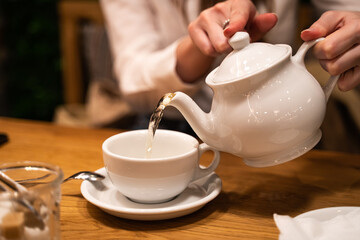 Close up hand pouring tea water from teapot to mug. Defocused background